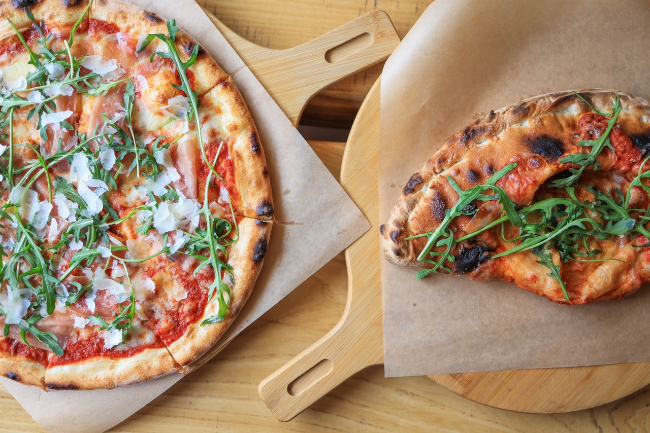 about-img Freshly baked pizzas topped with prosciutto, arugula, and cheese, served on wooden boards.