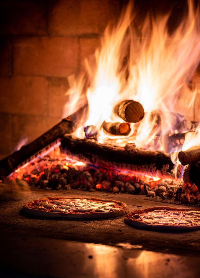 our-mission Delicious pizzas cooking in a traditional wood-fired oven, radiating warmth and flavor.