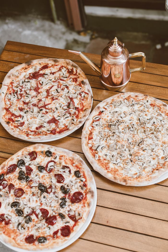 Close-up of three Italian pizzas on a wooden table with a copper pot for an appetizing food presentation.
